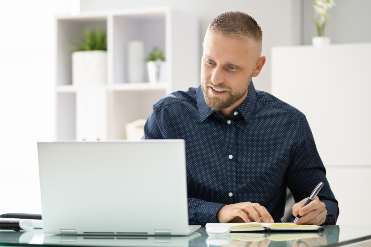 A man takes notes while watching a webinar.