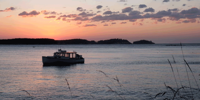 A small boat moored on the ocean at sunrise as seen from the coast
