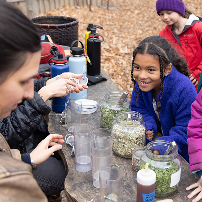 A group of young children make tea at an outdoor table