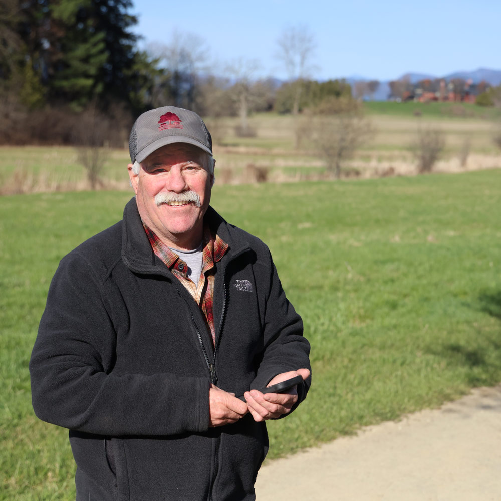 A man stands on a walking trail, green grass and blue skies in the distance.