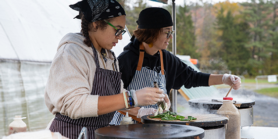 Two people make crepes under an outdoor tent