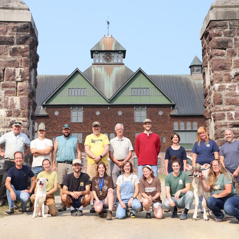 Group of people and with a dog and a calf posing in front of the Farm Barn on a sunny day.Group of people and with a dog and a calf posing in front of the Farm Barn on a sunny day