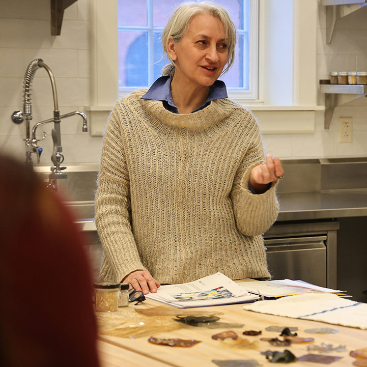 A woman in a sweater talks to a group in an industrial kitchen