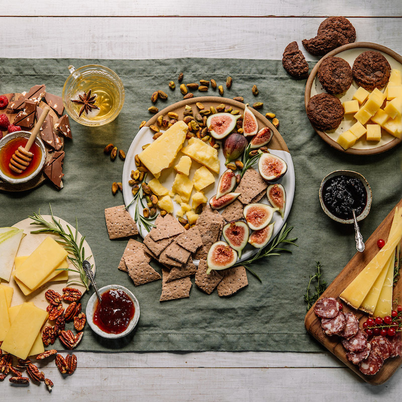 table with green runner full of plates of cheese and pairings