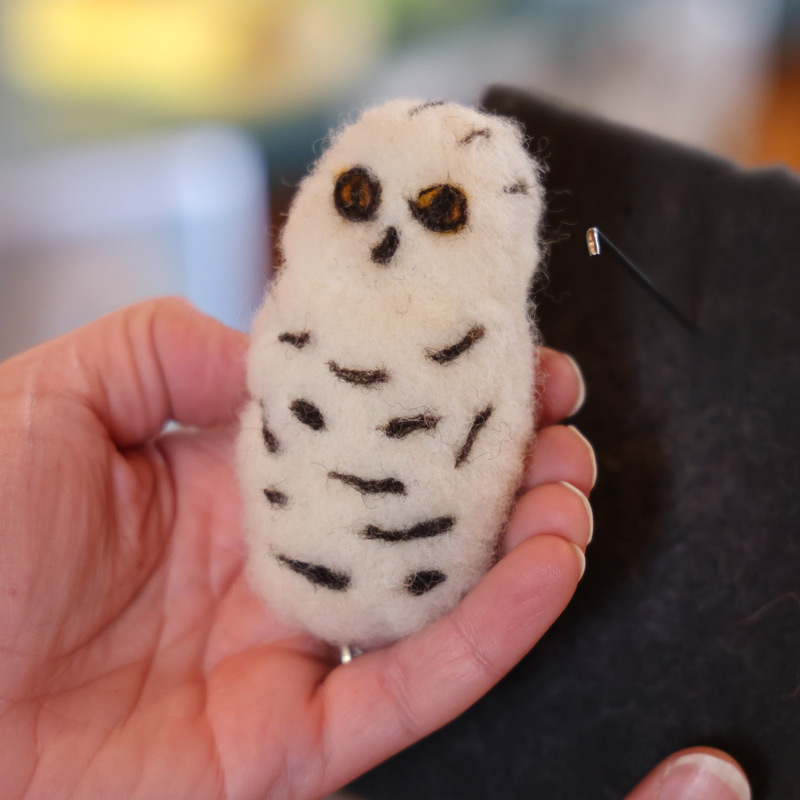 A person holds a white and black felted owl craft.