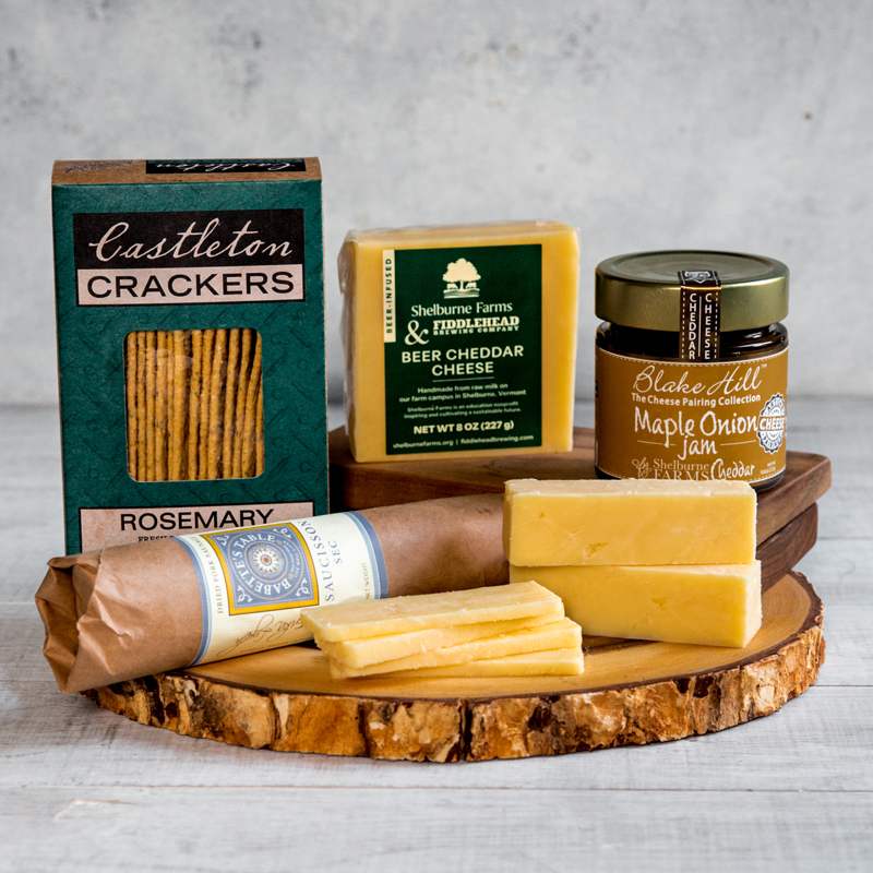Cheese, crackers, maple onion jam, and cured sausage arranged on a wooden board