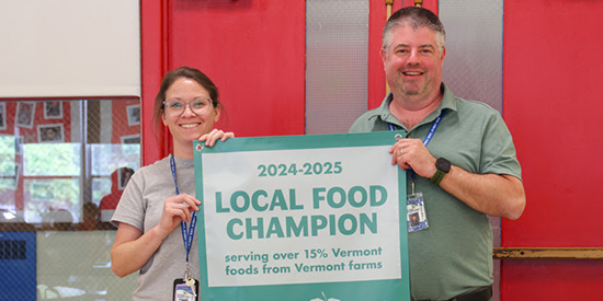 Two people smile while holding a banner that reads Local Food Champion