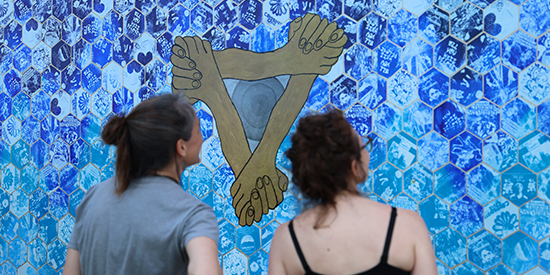 Two people admire a large mural depicting three interlocked hands