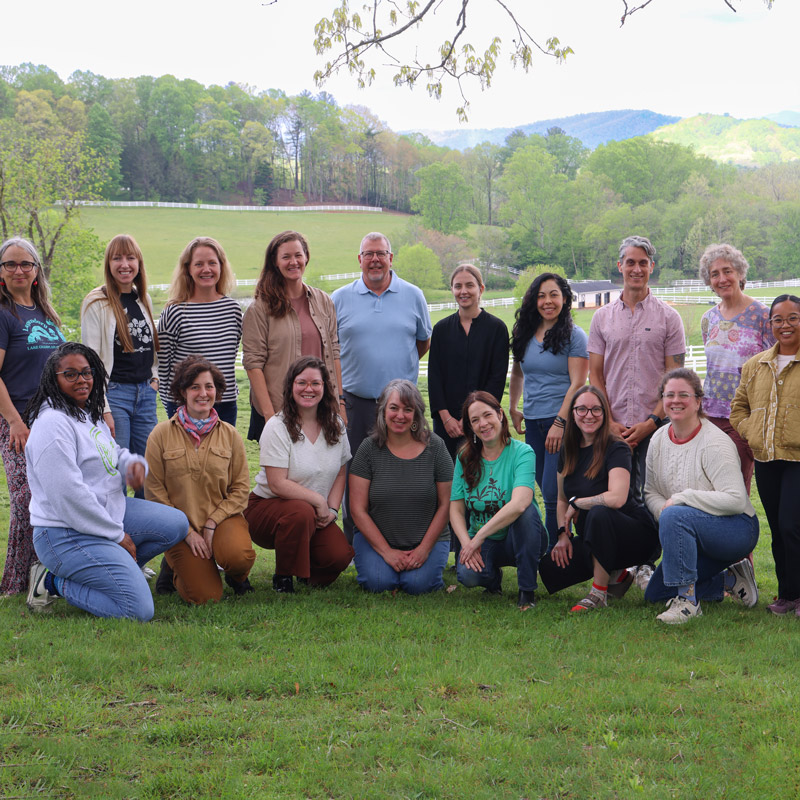 A large group of adults pose for a photo with a scenic farm landscape in the background.
