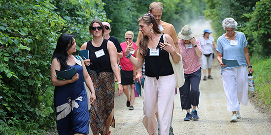 A group of adults walk down a dirt road while in conversation with lush greenery surrounding them