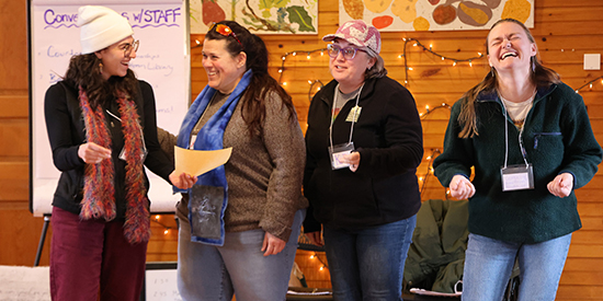 Four adults smile while standing in a wood paneled room performing poetry
