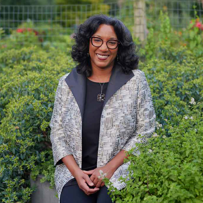 A woman smiles standing in a lush green garden