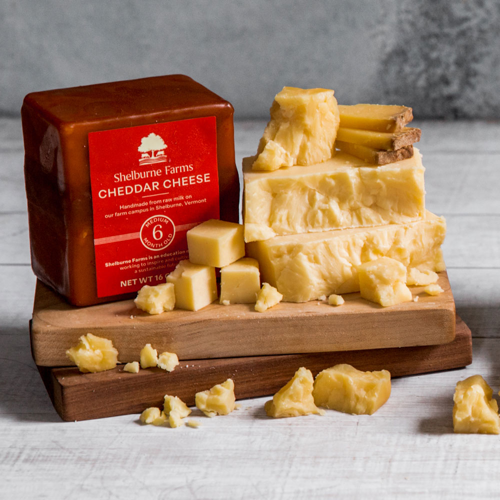 A wooden cutting board piled with various cheddar cheeses