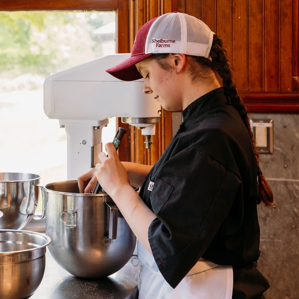 A pastry chef stirs a mixture in a large stainless steel bowl.