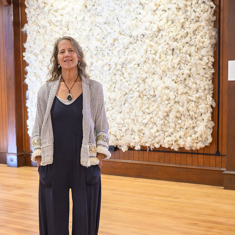 A woman stands in front of an artwork made of sheep's wool.