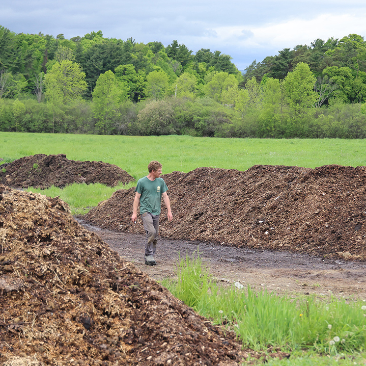 A man walks between two large rows of compost.