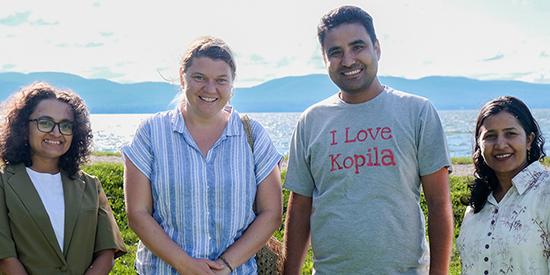 Four adults smile while standing on a lakeshore