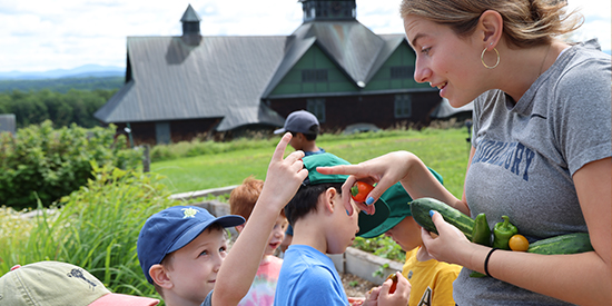A young child and educator stand in a garden holding vegetables