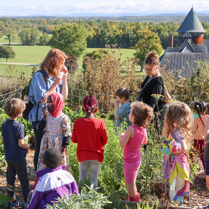 Two adults and a group of young children stand in a fall garden examining the crops.