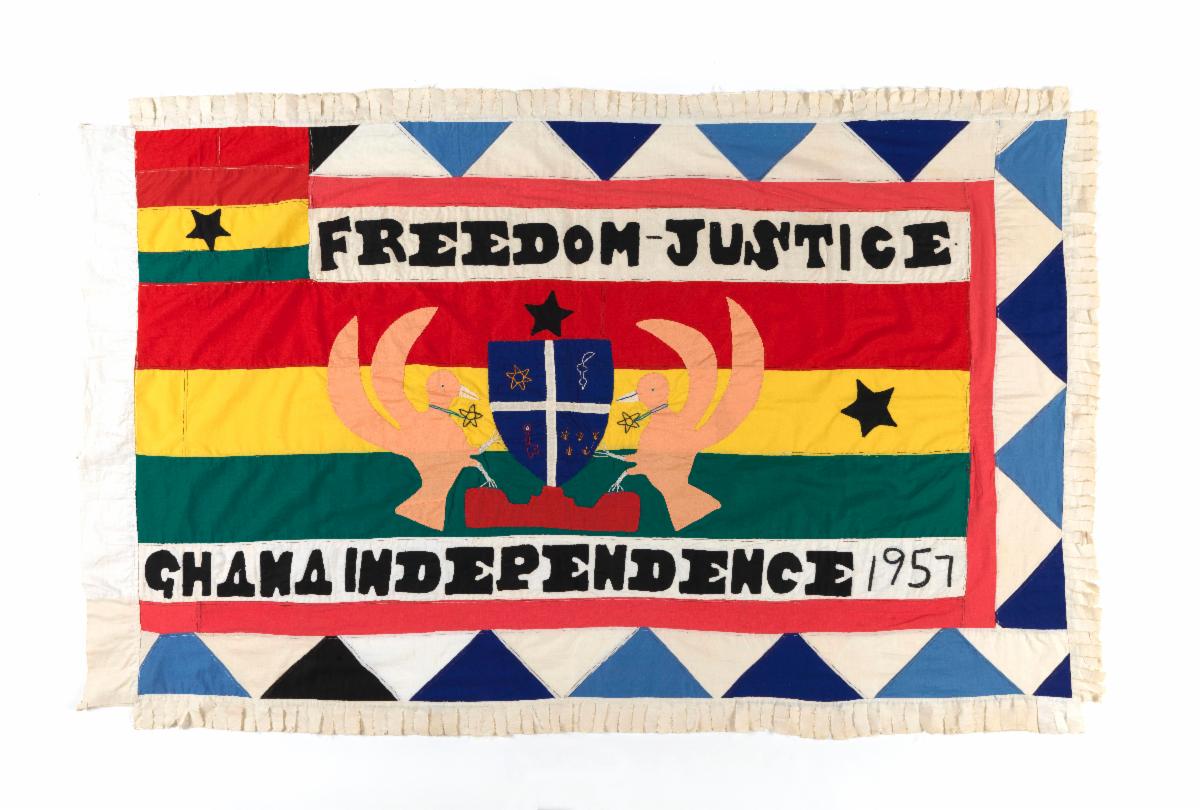 A colorful flag adorned with birds surrounding a coat of arms and the words: Freedom-Justice, Ghana Independence 1957