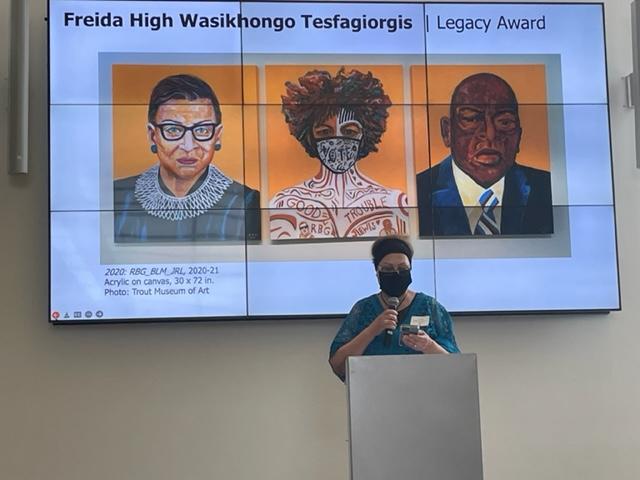 A woman standing at a podium in front of a projector screen with three images
