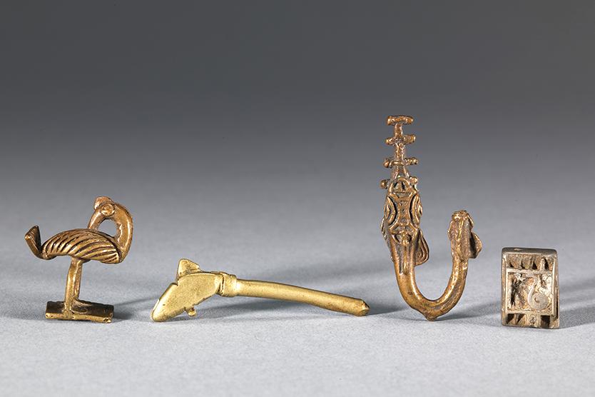 Four small copper alloy sculptures in the shape of a bird, a rifle, a sawfish, and a square piece with a swirl design