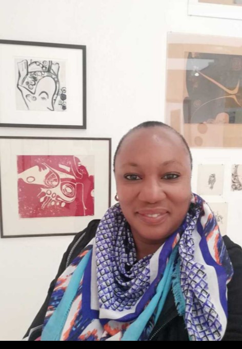 A smiling woman wearing colorful scarves in front of framed art