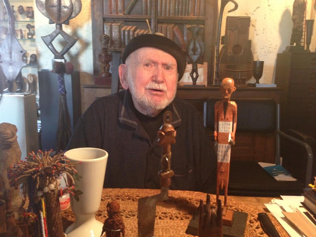 A bearded man in black hat surrounded by sculptures