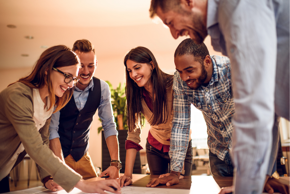A group of people standing around a table working together. 