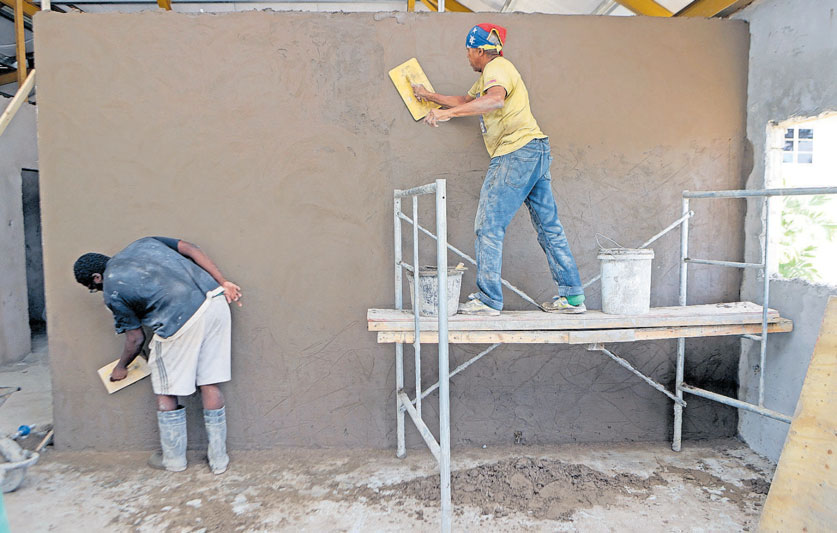 Construction workers Toby and Lorenzo plaster a wall with a mixture of cement and sand at a construction sitealong Alexandra Street, Port-of-Spain, yesterday. PHOTO BY LINCOLN HOLDER