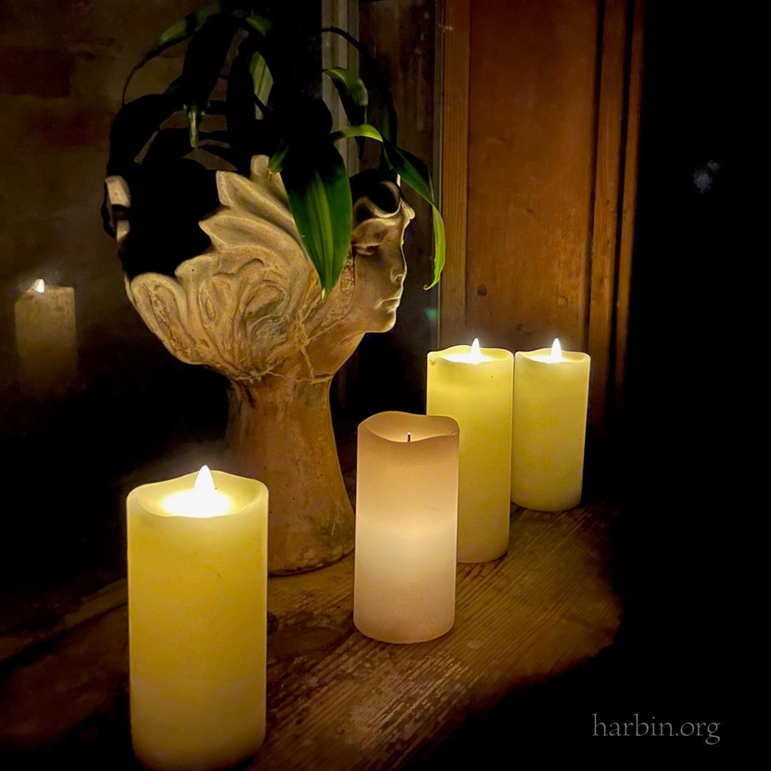 A statue of a face with a plant in the top sits with 4 thick white candles creating a glow in the dark space of the hot pool..