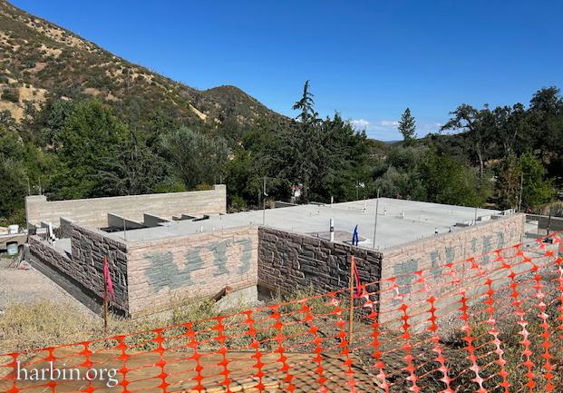 A newly built foundation for the restaurant with a blue sky and hills in the background. In the foreground is orange construction fencing.