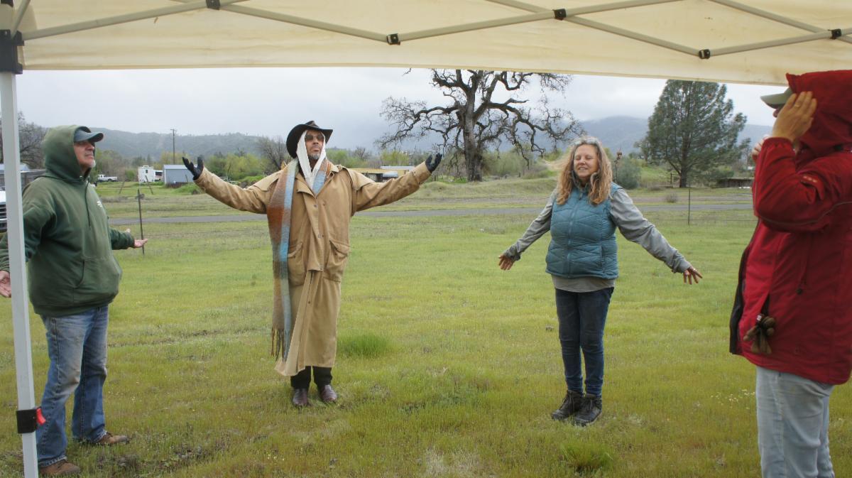 Four people stand in a circle in the misty rain on the farmland with arms open wide in a circle.