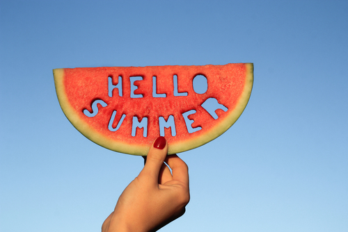 Watermelon slice  with text Hello Summer_  woman hands holding it against blue sky. Summertime concept.