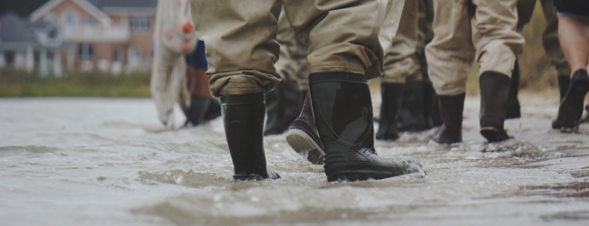 People wearing waders stand in a flooded street