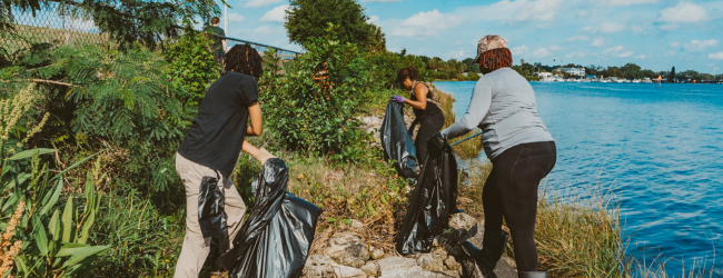 Three people pick up trash along the water's edge