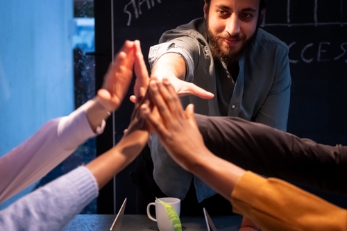 This vibrant and dynamic image captures a moment of celebration and teamwork. A group of individuals_ illuminated by warm_ intimate lighting_ is seen engaging in a high-five_ symbolizing success and