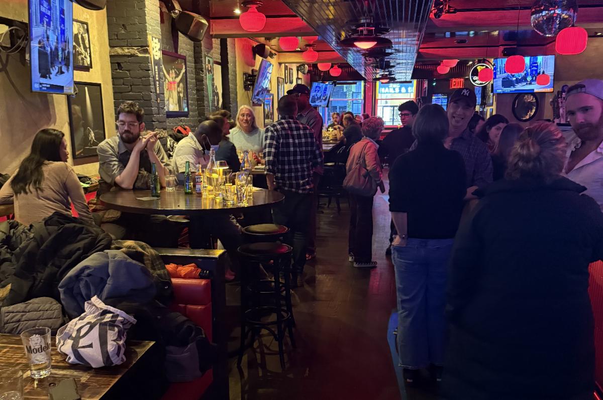 People gather in a darkened bar with deep red accent lights. 