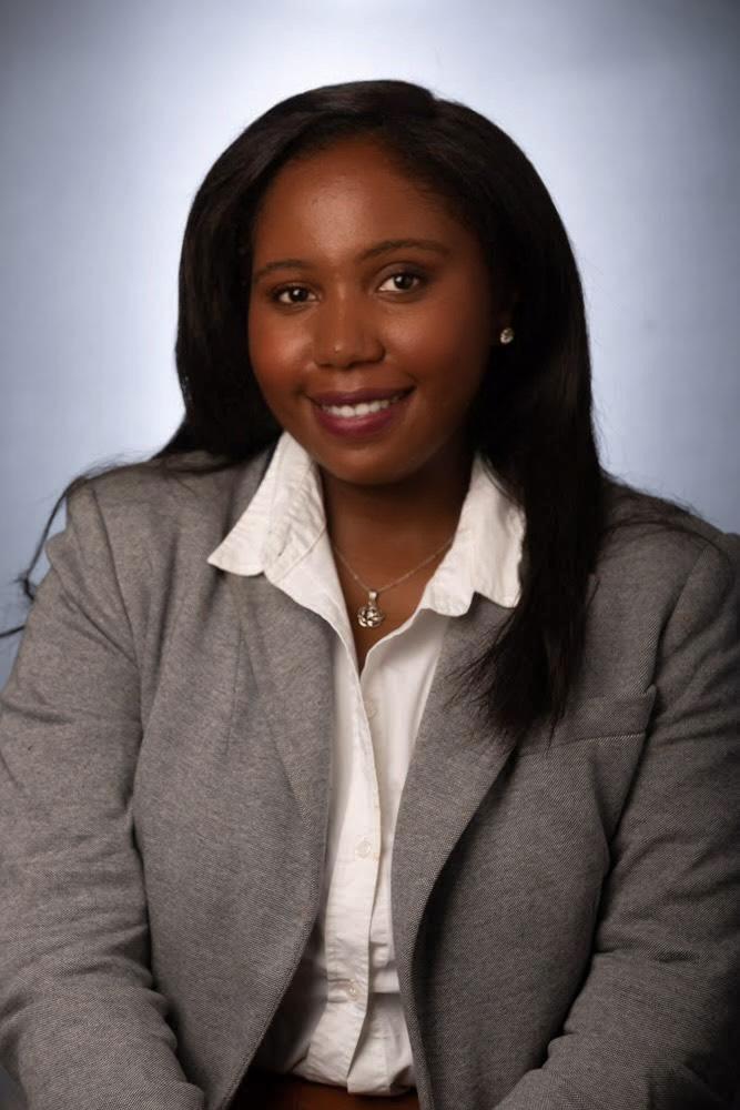 Daphne appears in a corporate headshot wearing a tweedy suit and a white button down shirt. 