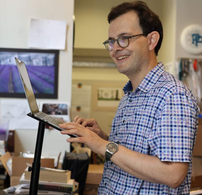 James is standing at a desk working on a computer. 