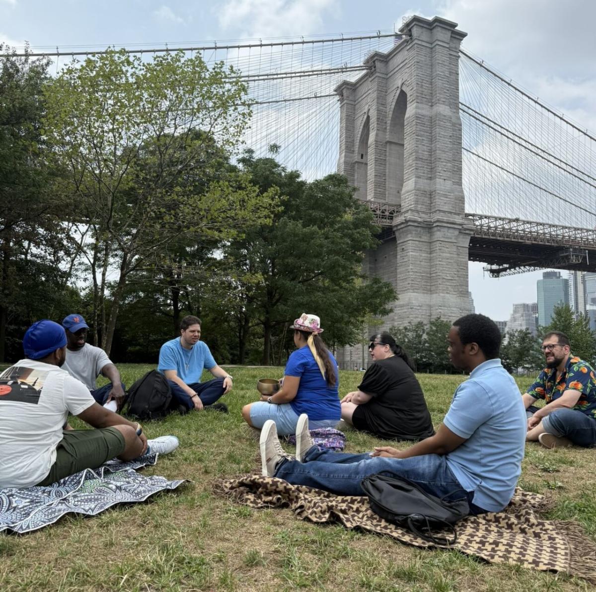 Job Path staff and participants sit on the grass with the Brooklyn Bridge in the background