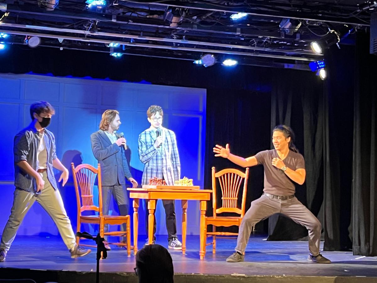Anson is one of several actors on a stage under stage lighting and he looks as if he's getting into a fighting stance. 