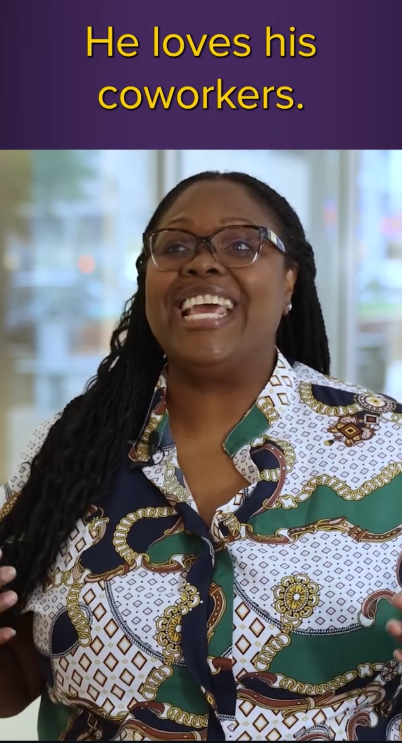 Taijii is wearing a brightly colored shirt with black, green, and gold and is smiling broadly. Above her are the words: He loves his coworkers.