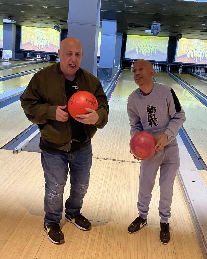Cornell and Steven stand with bowling balls posing at the bowling alley. 