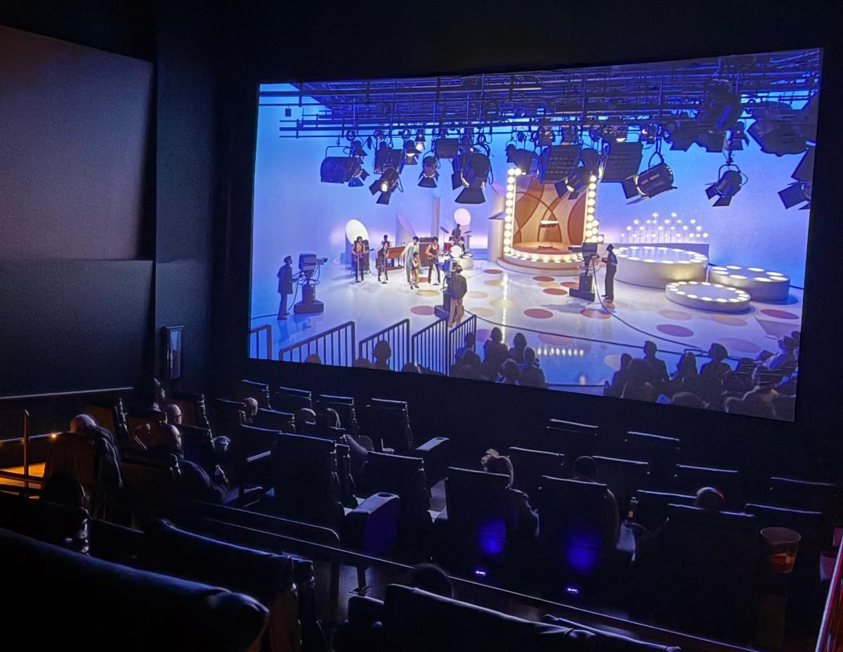 A movie screen shows a scene from the Michael Jackson movie with the audience in darkness. 