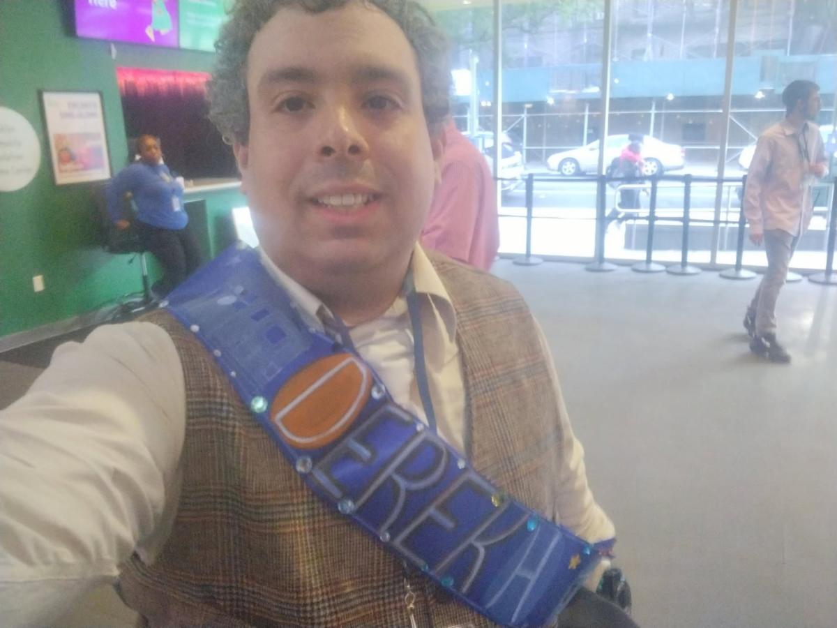 Derek smiles in a selfie wearing a bright blue congradulatory sash. 