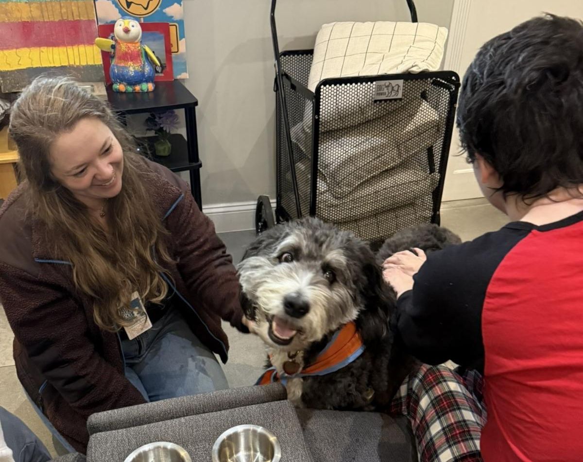 Ashley and Beto the dog are both smiling and you can see the back of a resident Erica and her hands on the dog. 