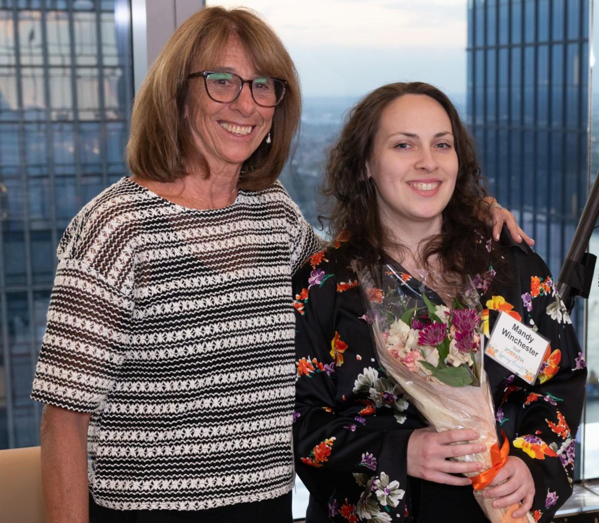 Abby and Mandy are standing in a room and Mandy is holding a bouquet of flowers. 