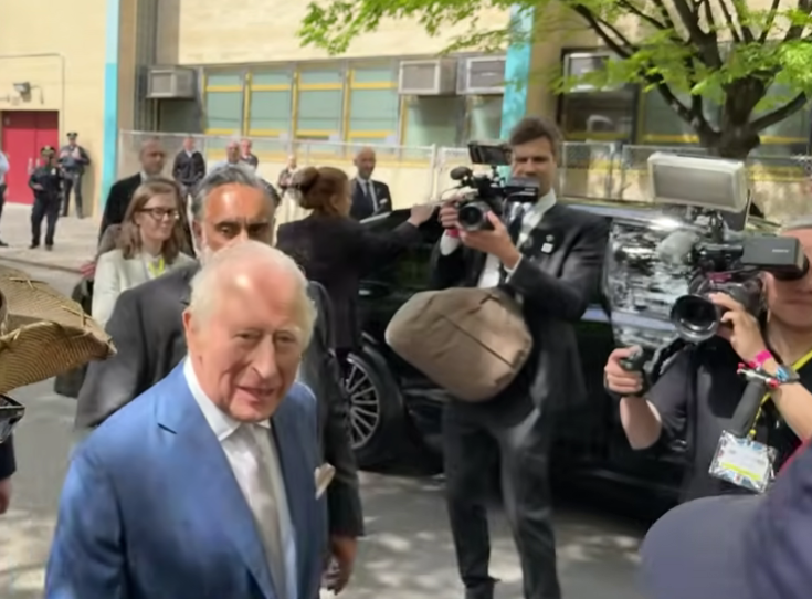 A still image from a video shows King Charles on a street surrounded by people taking photos and videos.