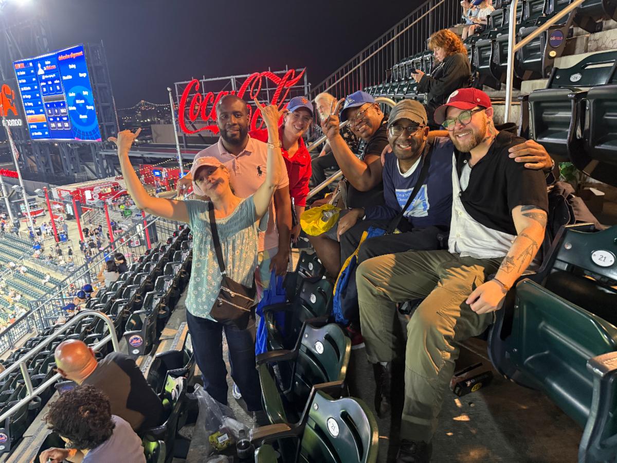 The group of people pose and smile in the stands of Citi Field. 